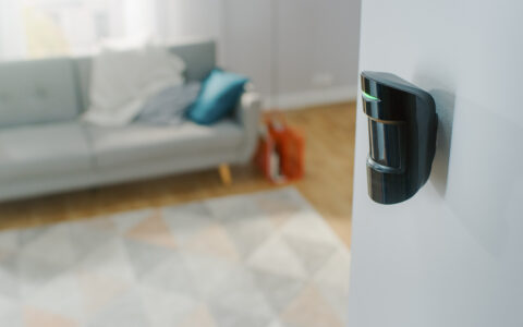 Close Up Object Shot of a Modern Movement Detector Unit on a White Wall in a Cozy Apartment in the Background.
